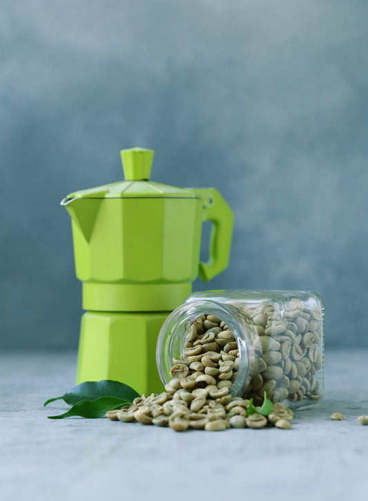 un bocal contenant des grains verts de café est ouvert, à côté une cafetière italienne de couleur verte